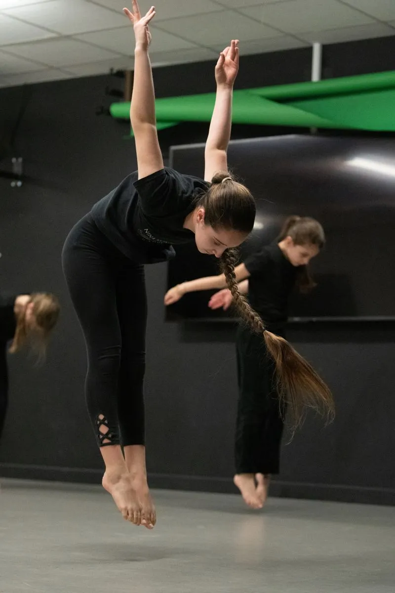 Contemporary dancer folding into a deep supported stretch while classmates move behind her