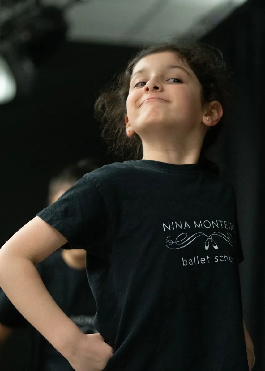 Young tap dancer standing proudly in the studio wearing a black academy shirt